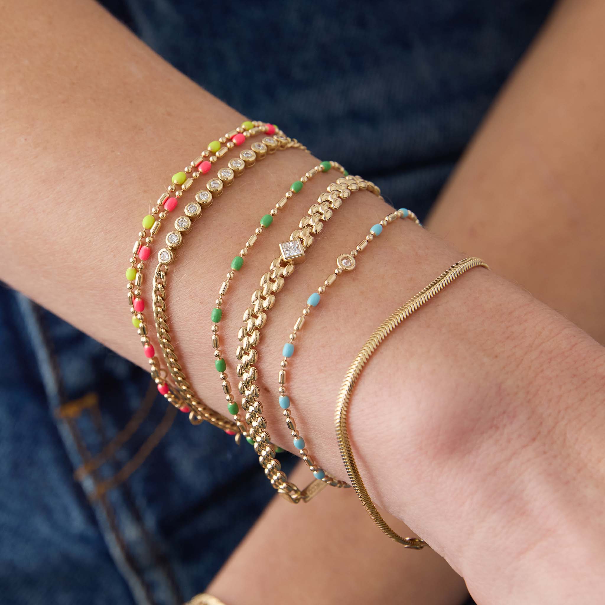 woman's wrist wearing a Zoë Chicco 14k Gold & Green Enamel Tube Bar Chain Bracelet stacked with Neon Pink and Neon Yellow versions and a 14k Floating Diamond Gold & Turquoise Enamel Tube Bar Chain Bracelet as well as a Small Snake Chain Bracelet, 14k Princess Diamond Small Panther Chain Bracelet, and 2mm Diamond Bezel Tennis Segment Bracelet