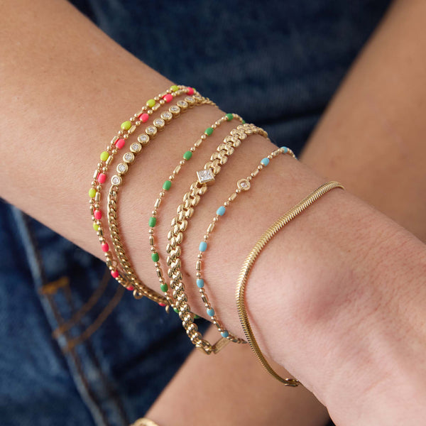 woman's wrist wearing a Zoë Chicco 14k Gold & Green Enamel Tube Bar Chain Bracelet stacked with Neon Pink and Neon Yellow versions and a 14k Floating Diamond Gold & Turquoise Enamel Tube Bar Chain Bracelet as well as a Small Snake Chain Bracelet, 14k Princess Diamond Small Panther Chain Bracelet, and 2mm Diamond Bezel Tennis Segment Bracelet