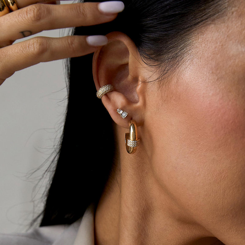 a close up of a woman's ear wearing a Zoë Chicco 14k Yellow Gold 3 Pavé Diamond Row Door Knocker Hoop Earring layered with a 14k Prong Pear & Emerald Cut Diamond Stud and a Pave Diamond Chubby Ear Cuff