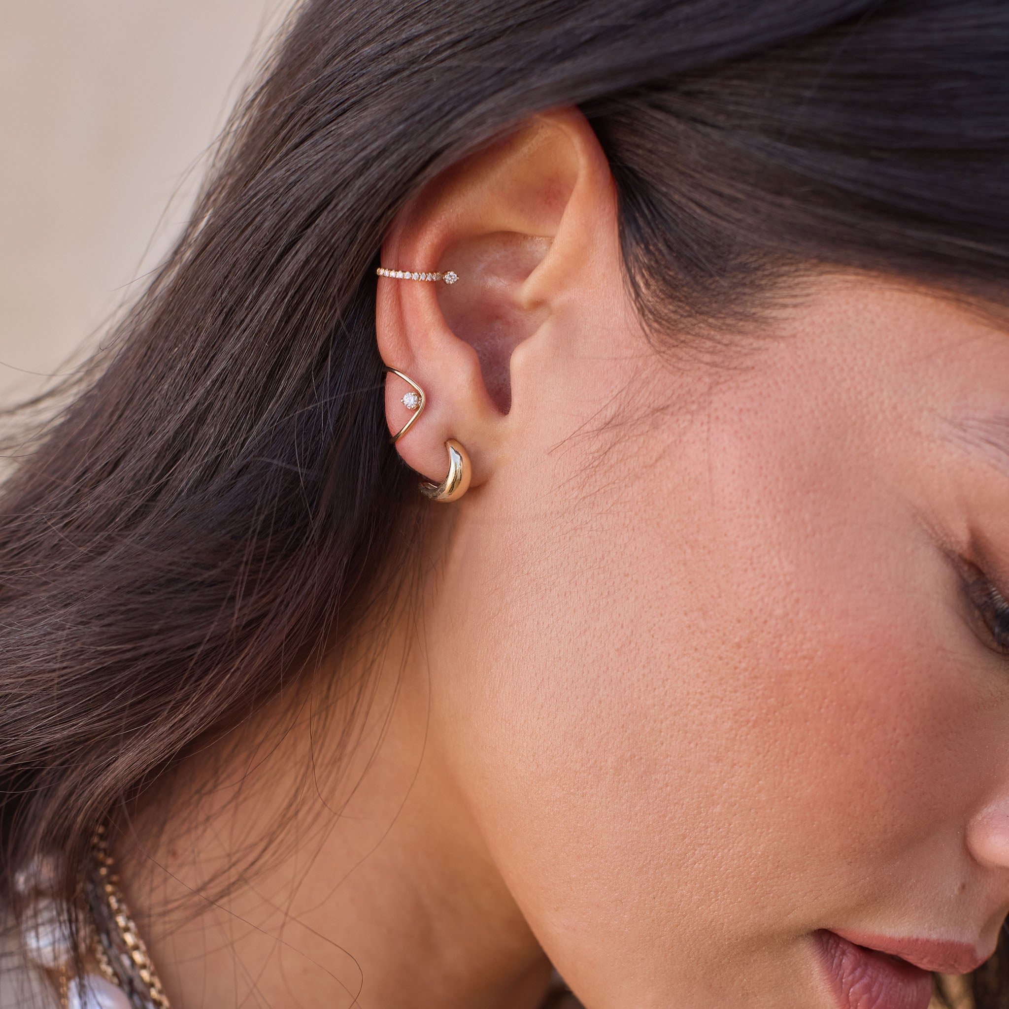 Woman wearing Zoe Chicco 14k gold wave and prong earring with a chubby gold hoop and diamond ear cuff
