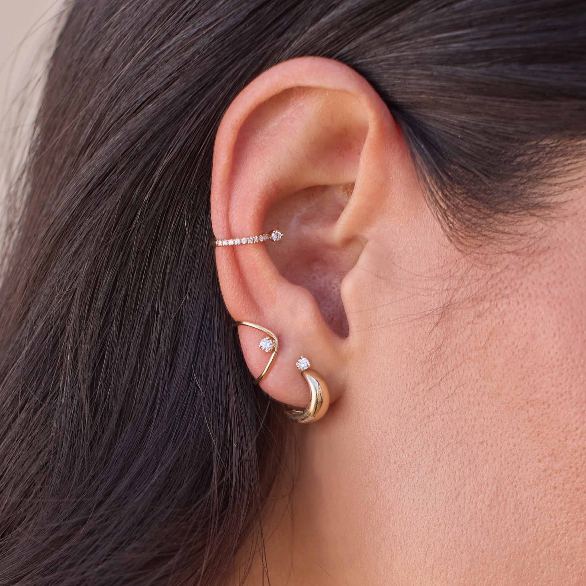 Close-up of an ear with Zoe Chicco 14k gold hoop earrings and ear cuffs with diamonds