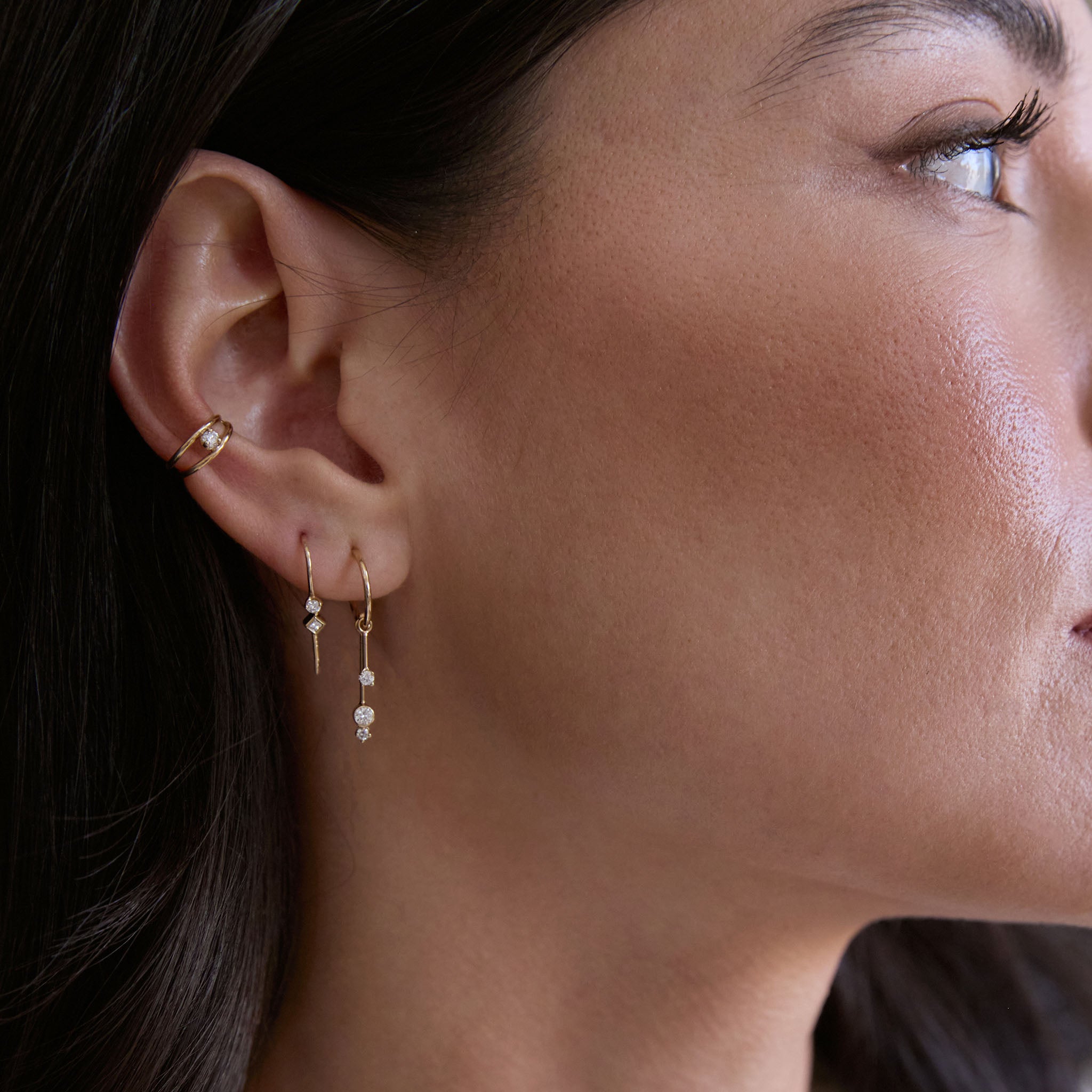 Close-up of woman wearing Zoe Chicco 14k gold and diamond dangle hoop earrings with an ear cuff