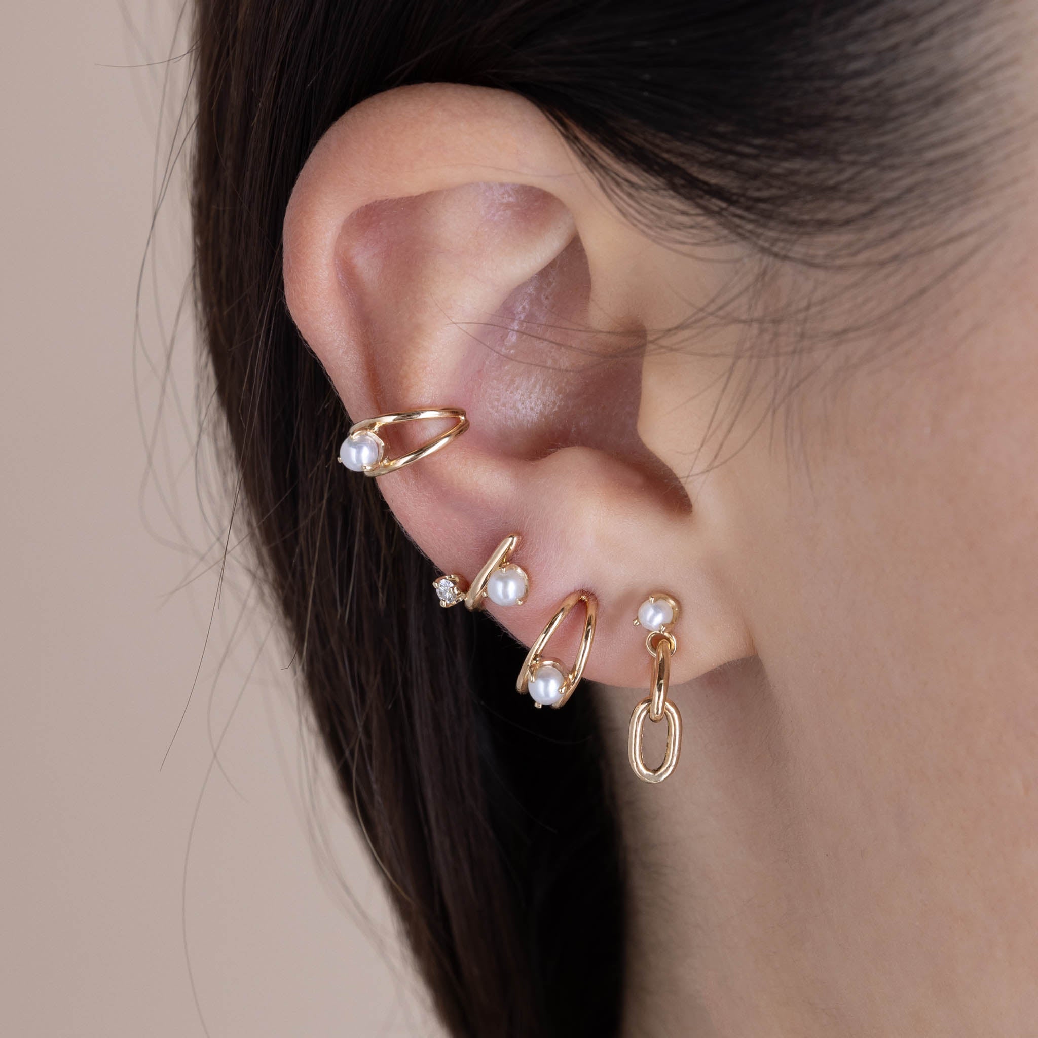 A woman's ear wearing a Zoë Chicco 14k Gold Mixed Prong Pearl & Diamond J Hook Hoop Earring in her third piercing layered with a 14k Pearl & Large Square Oval 2 Link Drop Earring, 14k Nested Pearl Double Wire Huggie Hoop, and a 14k Nested Pearl Double Wire Ear Cuff
