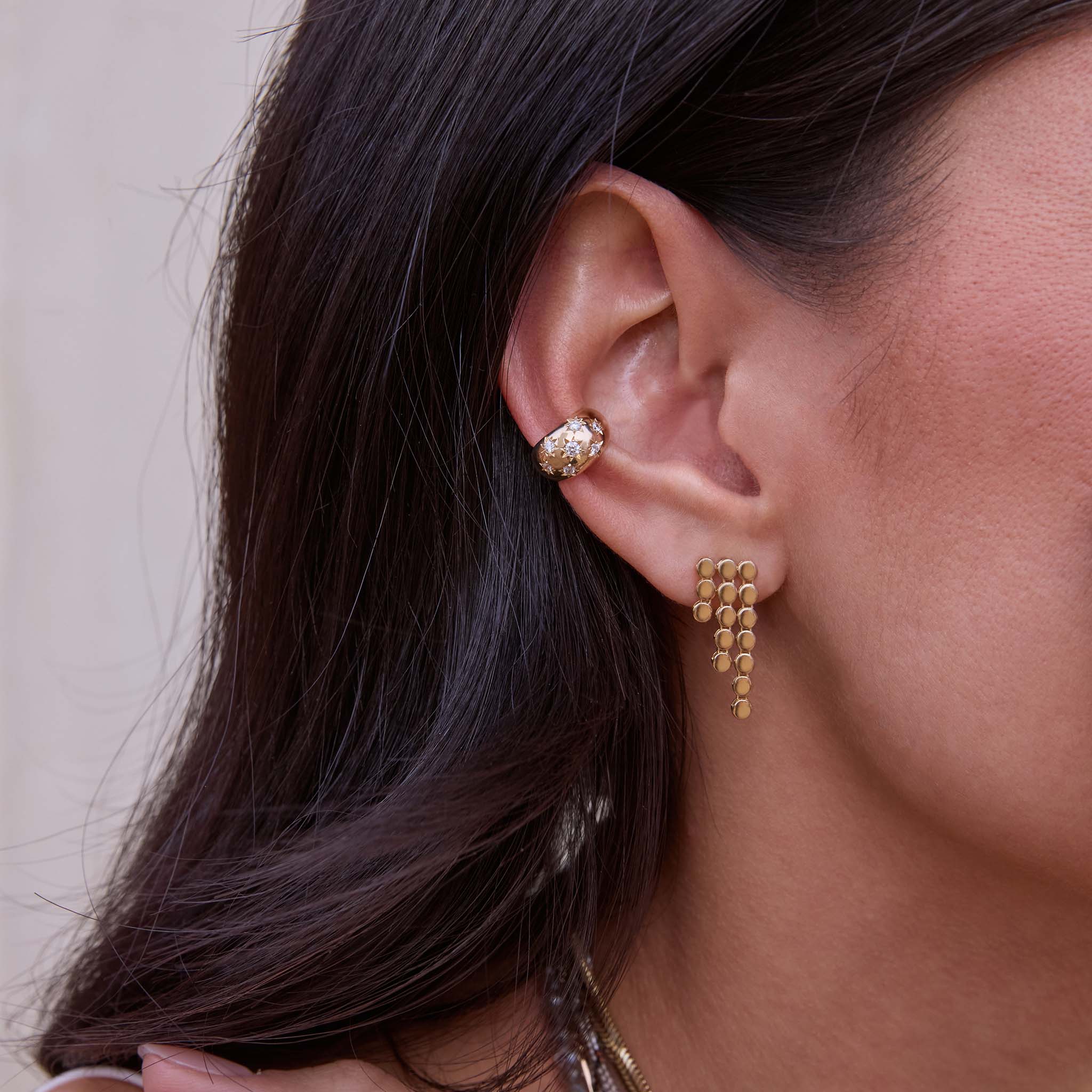 Close-up of a person wearing a Zoe Chicco 14k gold and star set diamond ear cuff with a puffed round waterfall chain earring with a neutral background 