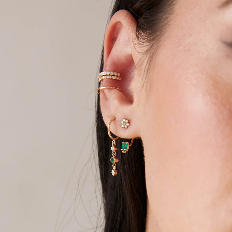 a close up of a woman's ear against a beige background wearing a Zoë Chicco 14k Gold Dangling Mixed Diamond & Emerald Hoop Earring in her second piercing