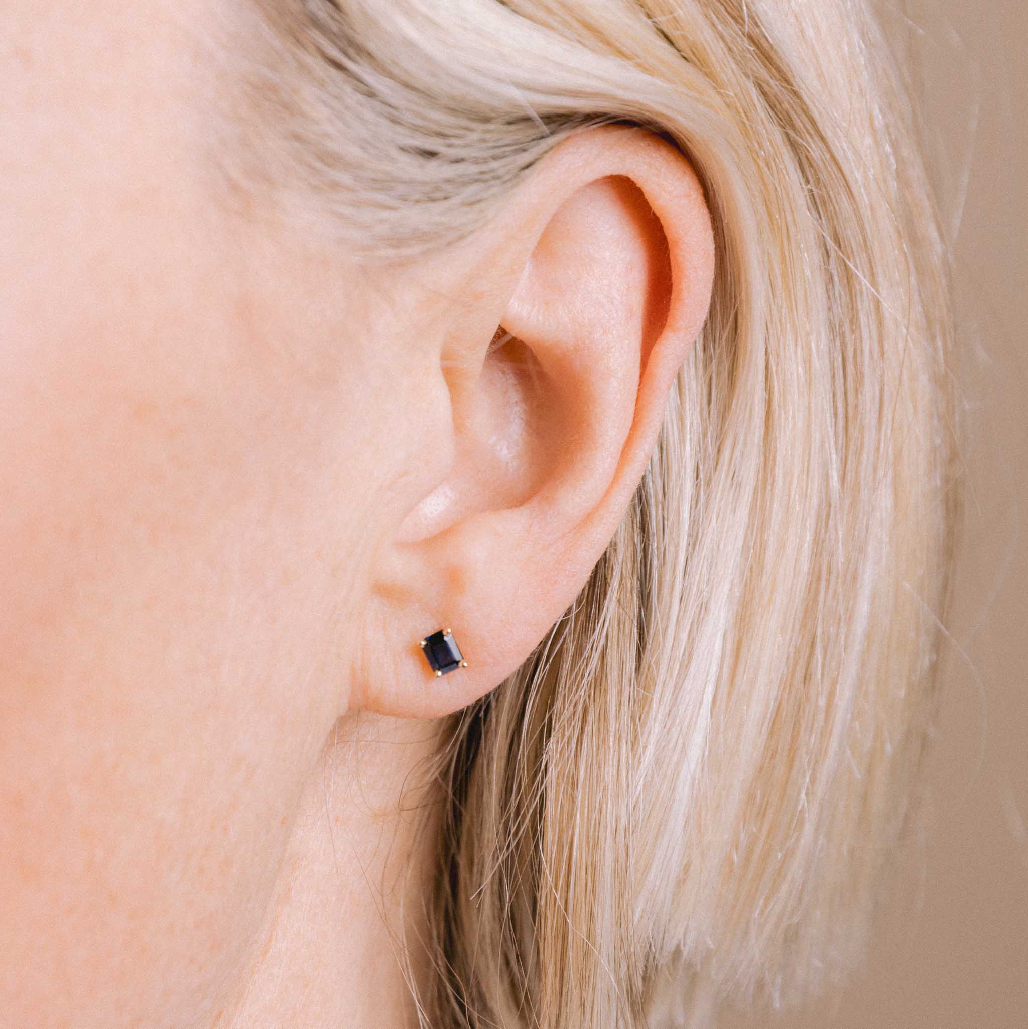 close up image of a woman's ear wearing a Zoë Chicco 14k Gold Emerald Cut Blue Sapphire Stud Earring