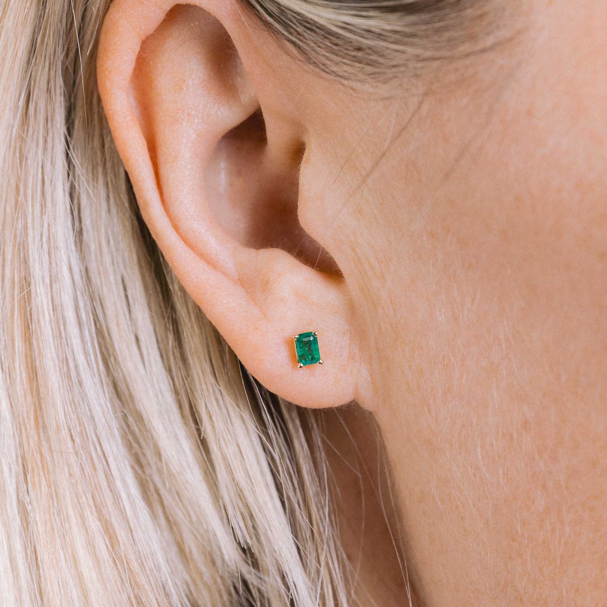 A woman with blonde hair wears the emerald-cut emerald stud earrings.