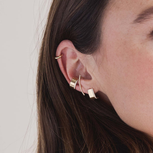 woman's ear wearing a Zoë Chicco 14k Gold Wide Flat J Huggie Hoop Earring layered with a 14k Wide Flat Ear Cuff and a 14k Pavé Diamond Thick Wire Bar Ear Cuff