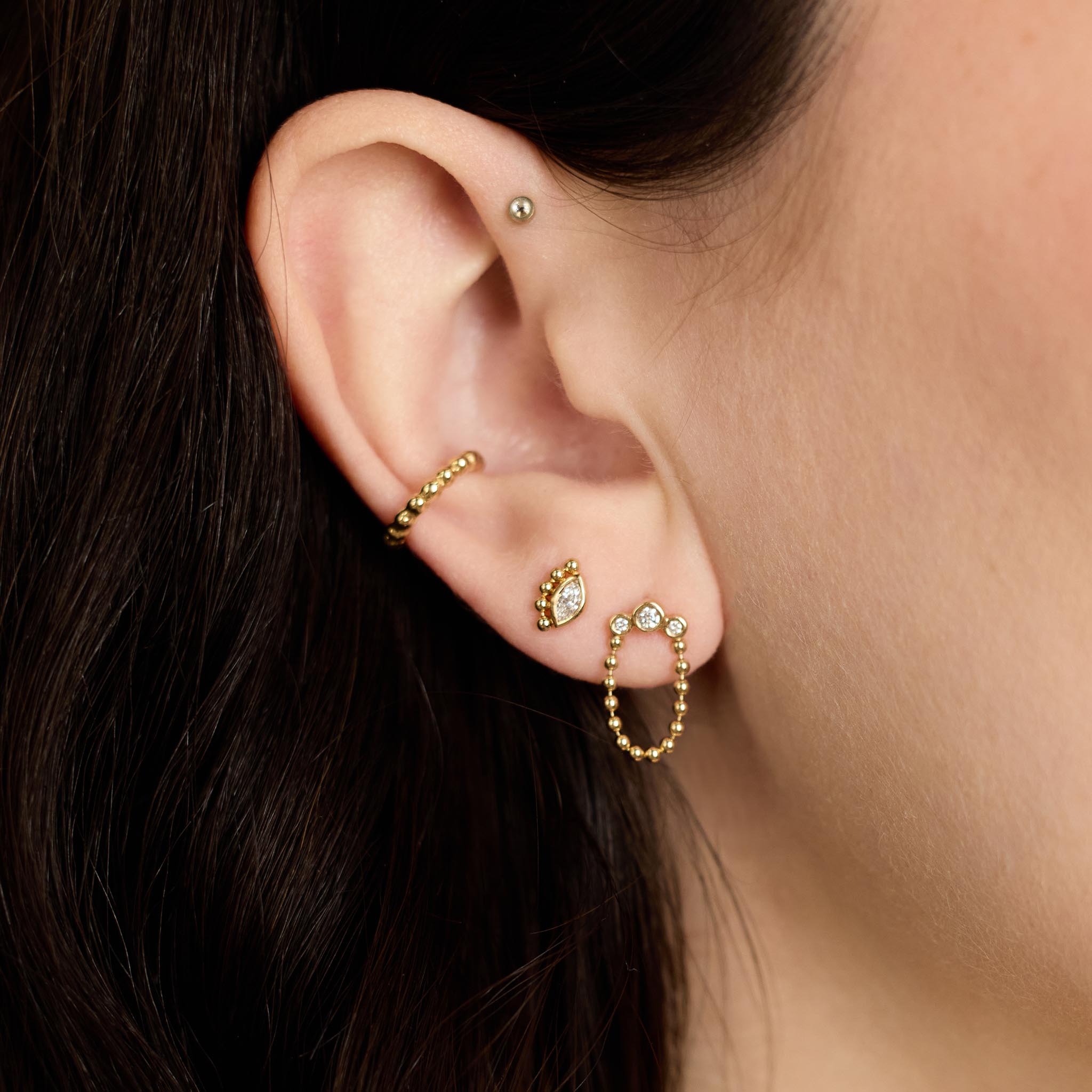 Close-up of an ear wearing multiple Zoe Chicco 14k gold and diamond bead earrings with a blurred background