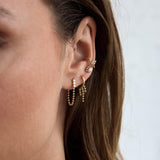 close up of a woman's ear wearing a Single Zoë Chicco 14k Gold Waterfall Bead Chain Hinge Huggie Hoop Earring in her second piercing layered with a 14k Beaded Marquise Diamond Bezel Stud and a 14k Prong Diamond Trio Thick Ear Cuff
