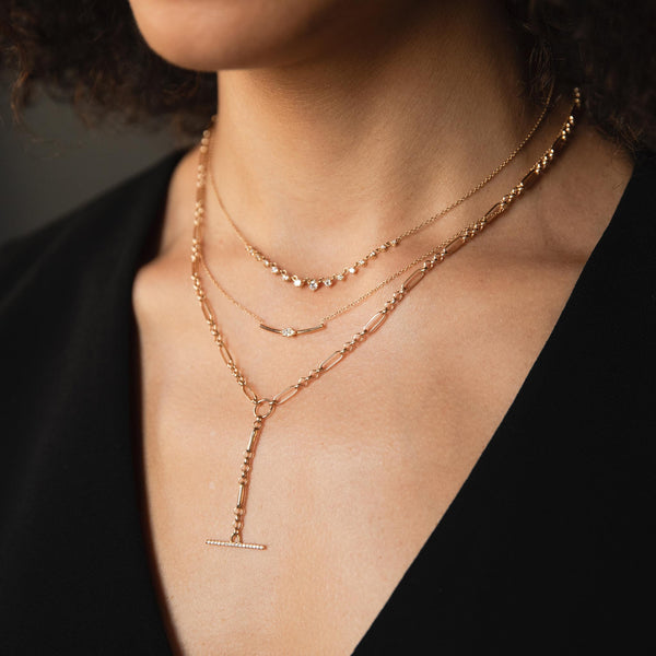 A woman wears a Zoe Chicco necklace stack including a graduated linked prong diamonds, bar with marquise diamond and a rolo/paperclip lariat with a pave diamond toggle bar.
