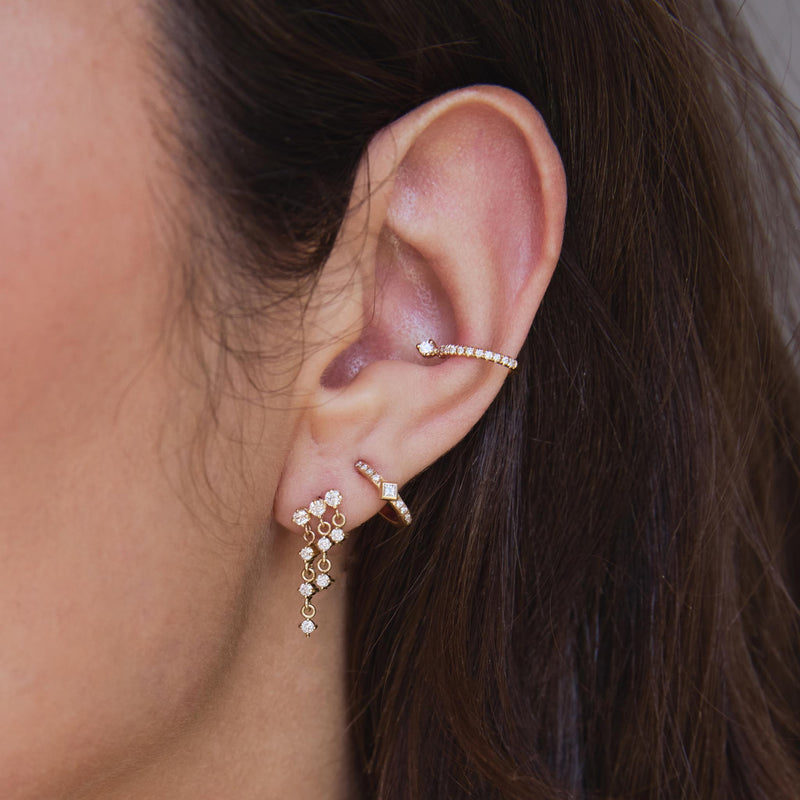 close up of a woman's ear wearing a Zoë Chicco 14k Gold Linked Prong Diamond Waterfall Earring layered with a 14k Princess Diamond & Diamond Bar Huggie Hoop