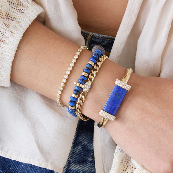 Close-up of a wrist wearing multiple bracelets with blue and gold accents featuring 14k Large Lapis & Pavé Diamond Bar Half Round Cuff