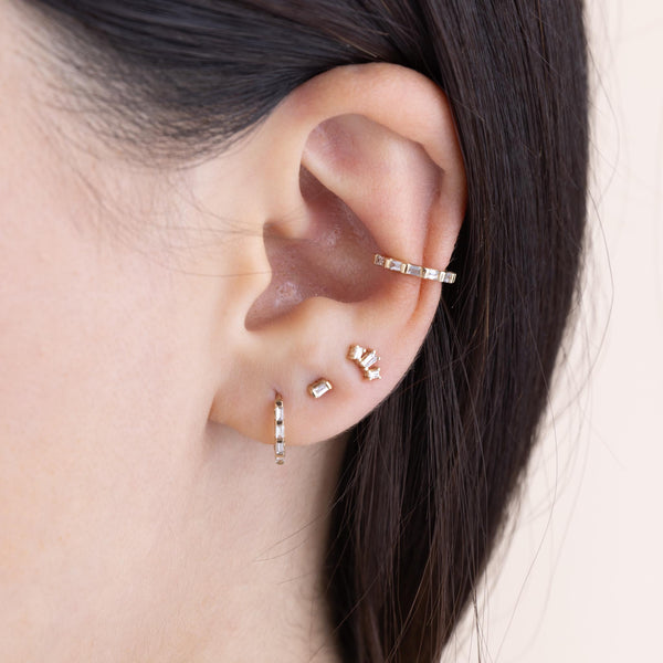 woman's ear wearing a Zoë Chicco 14k Gold Tapered Baguette Diamond Fan Stud Earring in her third piercing layered with a Baguette Diamond Stud, Baguette Diamond Hinge Huggie Hoop, and a Baguette Diamond Eternity Ear Cuff