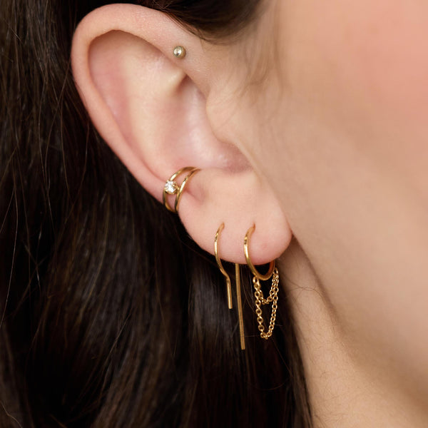 close up of a woman's ear wearing a Zoë Chicco 14k Gold Wire Hook Earring in her second piercing layered with a 14k Double Chain Loop Thin Huggie Hoop and a Nested Prong Diamond Ear Cuff