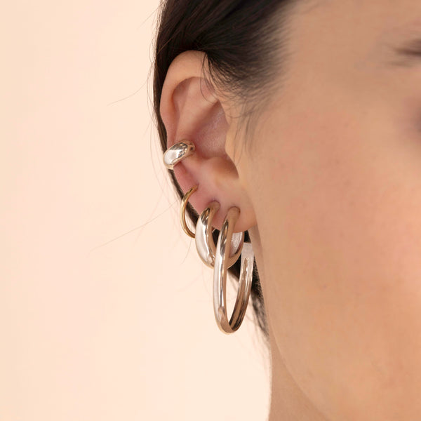 A model wears Sterling Silver Large Chubby Hoops, Sterling Silver Medium Aura Huggie Hoops and Sterling Silver Wide Chubby Ear Cuff