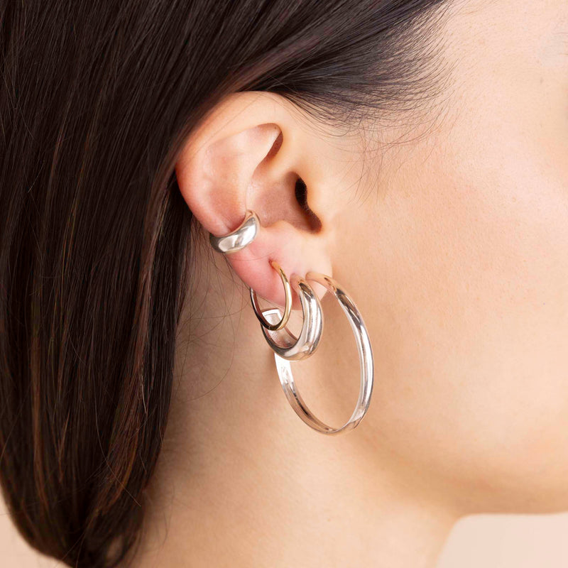 A model wears Sterling Silver Large Chubby Hoops, Sterling Silver Medium Aura Huggie Hoops and Sterling Silver Wide Chubby Ear Cuff