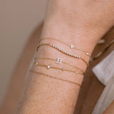 A woman wears a stack of Zoe Chicco 14k bracelets including 14k Itty Bitty Pavé Diamond Heart Bracelet with Floating Diamond, tennis segment bracelet, block letter bracelet and stationed baguettes