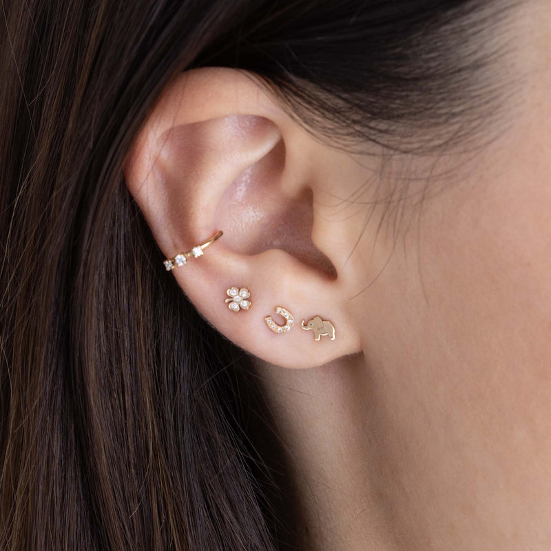 woman's ear wearing a Zoë Chicco 14k Gold Itty Bitty Diamond Clover Stud Earring in her third piercing layered with an Itty Bitty Elephant Stud and an Itty Bitty Pavé Diamond Horseshoe Stud Earring