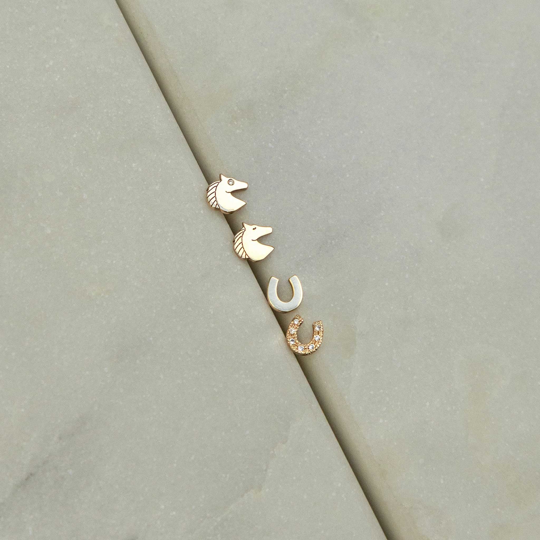Set of gold itty bitty horse and horseshoe stud earrings on a marble background