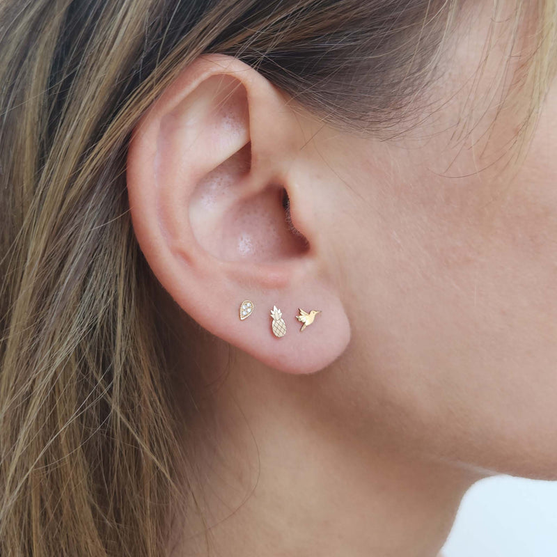 Close up of a woman's ear wearing a Zoë Chicco 14k Gold Itty Bitty Pineapple Stud Earring in her second piercing and a 14k Itty Bitty Hummingbird Stud in her first piercing