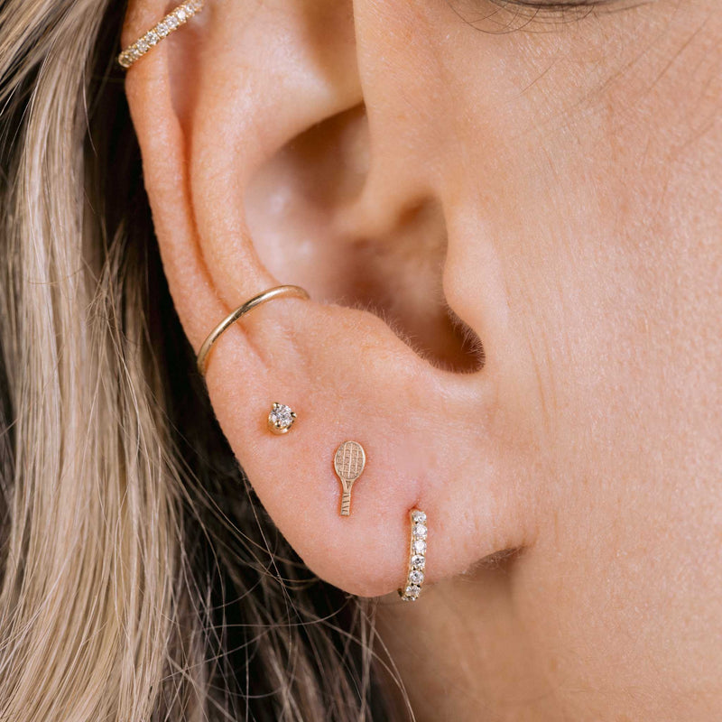 close up of a woman's ear wearing a Zoë Chicco 14k Gold Itty Bitty Tennis Racket Stud Earring in her second piercing layered with a small diamond stud and a Pave Diamond Huggie Hoop