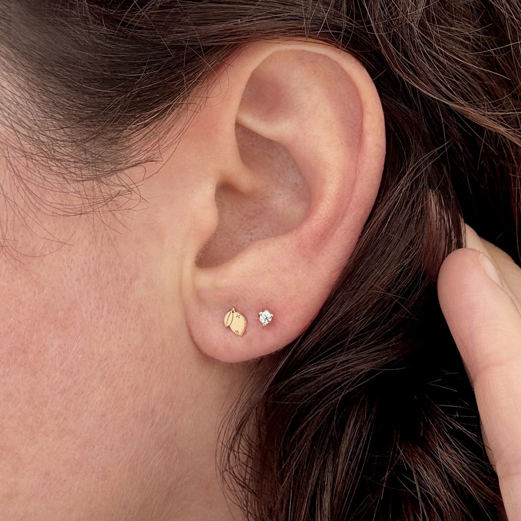 Close-up of an ear wearing 14k gold Zoe Chicco itty bitty lemon stud earring and a prong diamond stud earring