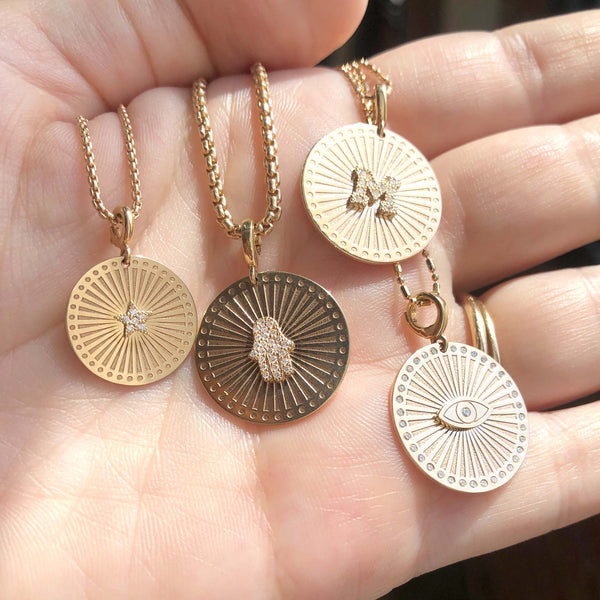 woman holding a Zoë Chicco 14k Gold Diamond Evil Eye Medium Sunbeam Medallion Necklace in her palm with three other medallion necklaces