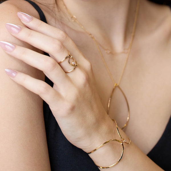 Close-up of a hand wearing Zoe Chicco 14k gold jewelry including a ring, bracelet, and necklace.