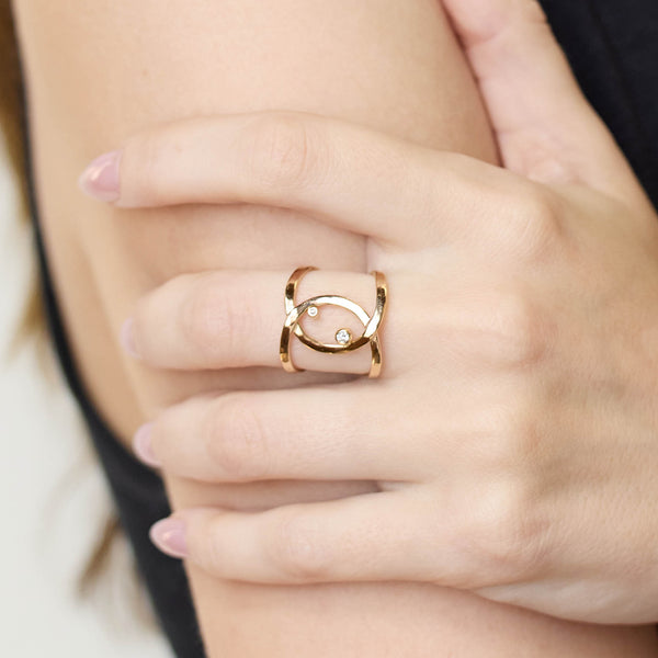 Close up of a hand wearing a Zoe Chicco 14k gold infinity ring with 2 small diamonds on a blurred background