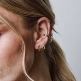 woman's ear wearing a Zoë Chicco 14k Gold Prong Diamond Knife Edge Hinge Huggie Hoop Earring layered with a 14k Two Tone Double Wire Huggie Hoop and 14k Diamond Tennis Short Drop Earring in her other piercings and a 14k Marquise Diamond Chubby Ear Cuff
 