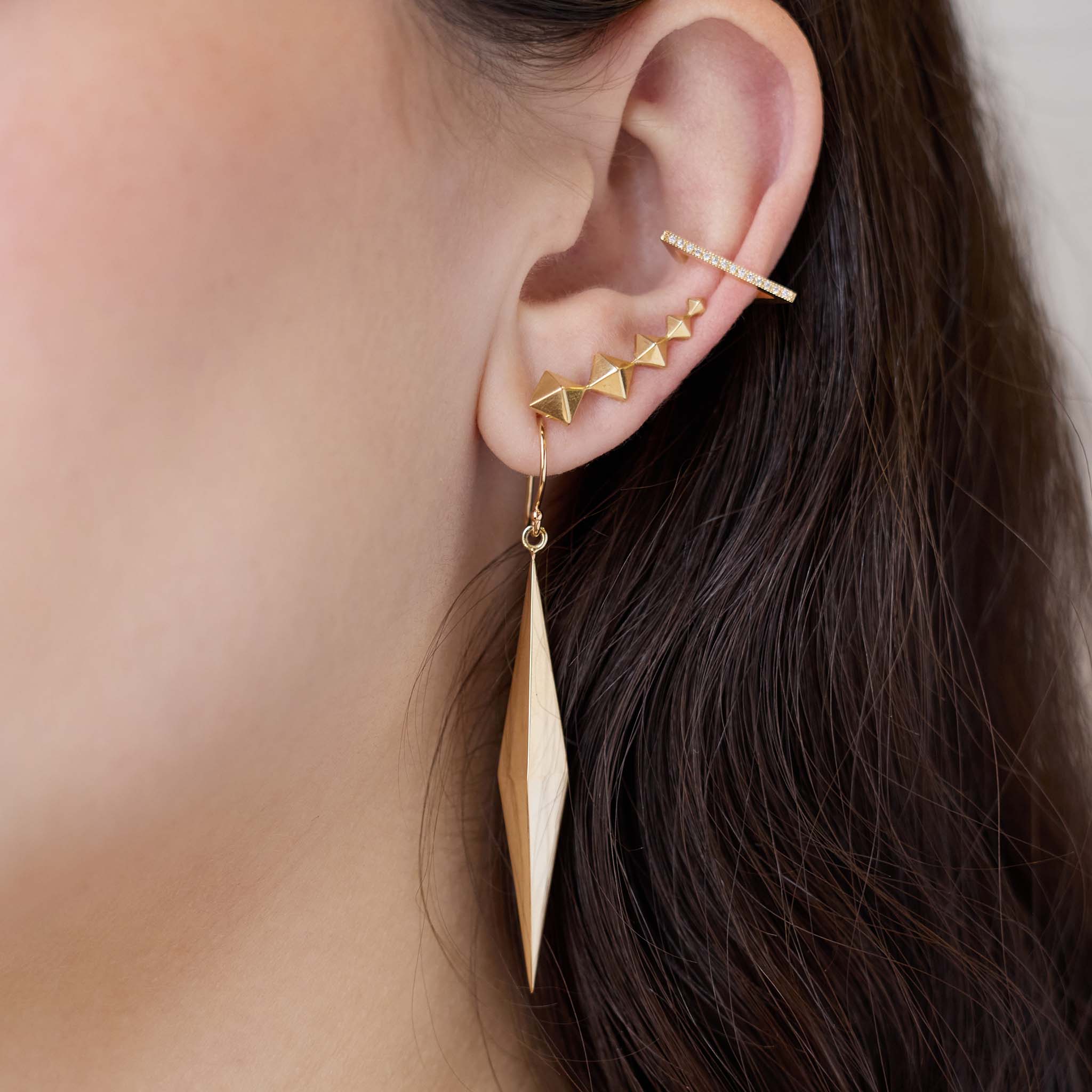 Close up of an ear wearing Zoe Chicco 14k gold geometric pyramid dangle earrings and ear adornments. 