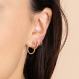 A model is wearing Zoe Chicco's 14k Two Tone Gold Reversible Hinge Huggie Hoops in size 17mm, 12mm and 10.5mm up the ear.