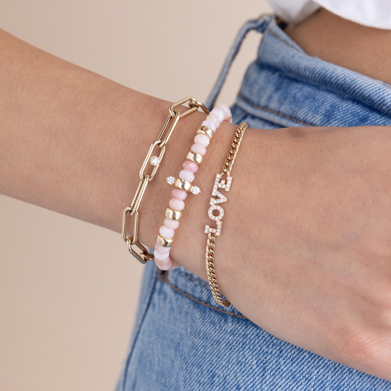 woman's wrist wearing a Zoë Chicco 14k Gold Single Diamond Large Paperclip Chain Bracelet stacked with a 14k Gold & Faceted Pink Opal Rondelle Bead Bracelet with 2 Prong Diamonds and a 14k Pavé Diamond LOVE Small Curb Chain Bracelet