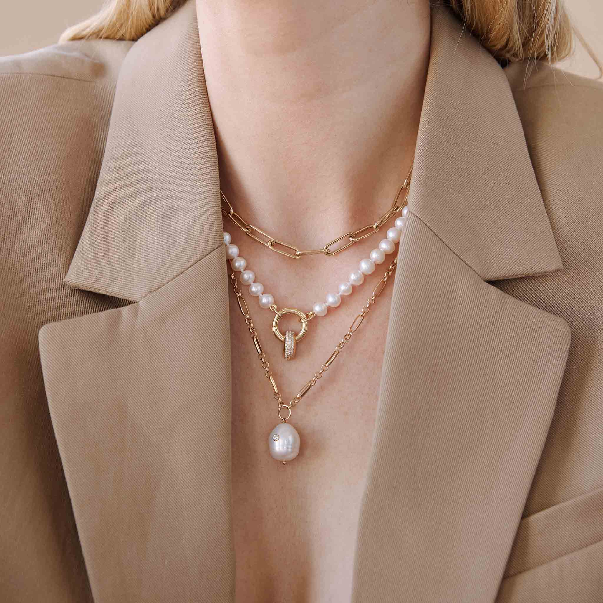 woman in a tan blazer wearing a Zoë Chicco 14k Gold Diamond Baroque Pearl Paperclip Rolo Chain Necklace layered with a Large Paperclip Chain Necklace and a 14k Medium Pearl Large Round Enhancer Necklace with a 14k Pavé Diamond Wide Half Round Slide Bead Charm 