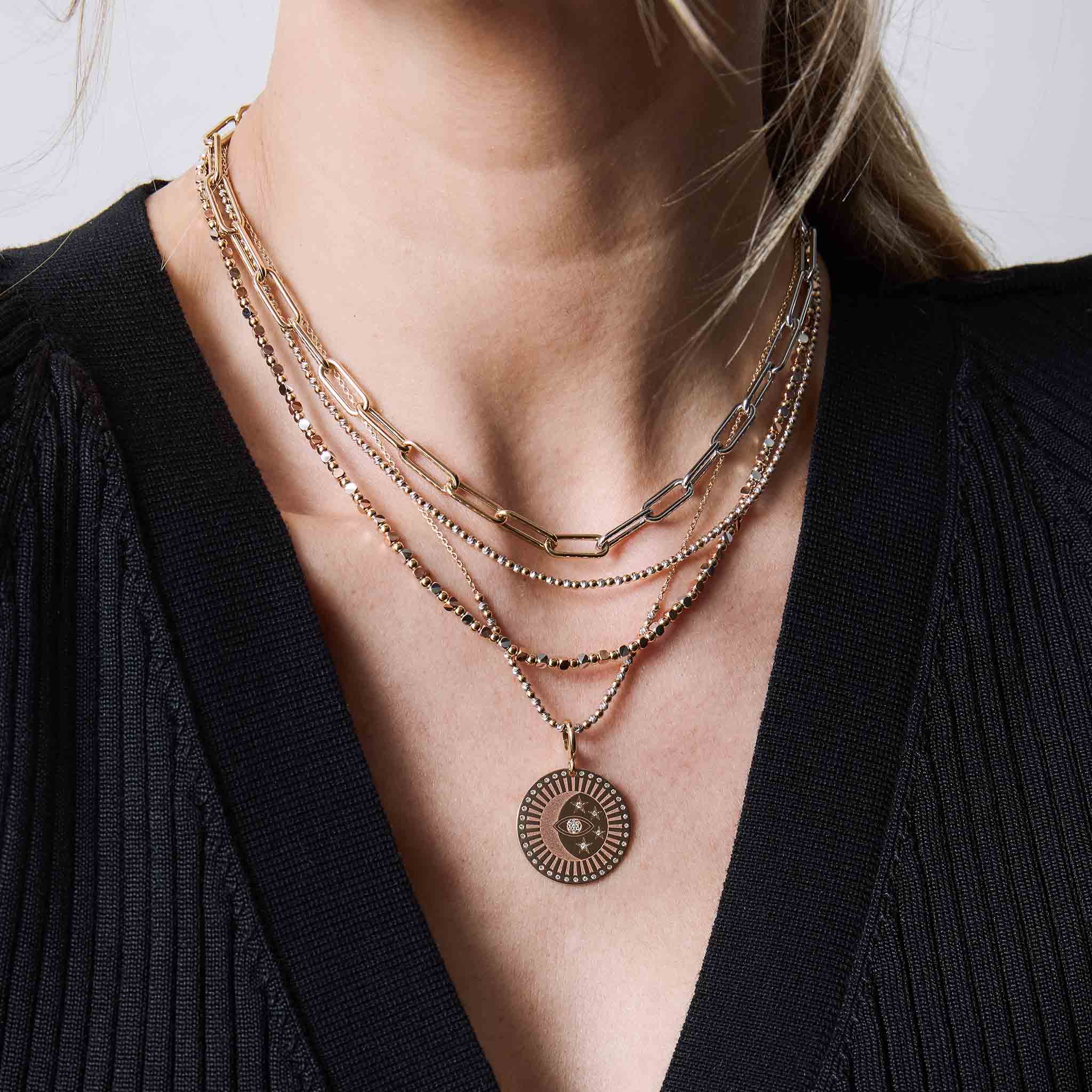 woman in a black sweater wearing a Zoë Chicco 14k Gold Two Tone Gold Large Paperclip Chain Necklace layered with bead necklaces and a 14k Single Large Celestial Protection Medallion Charm clipped onto one of the necklaces