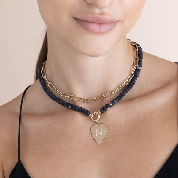 woman wearing a Zoë Chicco 14k Gold Matte Black Agate Rondelle Bead Round Enhancer Necklace with a Pavé Diamond Initial N Shield Pendant clipped onto the enhancer and layered with a Large Paperclip Chain Necklace