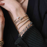 woman in a black sweater wearing a Zoë Chicco Sterling Silver Large Box Chain Bracelet layered with a Silver Large Mariner Chain Bracelet, Platinum Mixed Pear & Emerald Cut Diamonds with Pavé Diamonds Cuff, 14k Marquise Diamond Halo Tennis Bracelet, 14k Two Tone Gold Large Paperclip Chain Bracelet, and  a Baguette Diamond San Marco Chain Bracelet