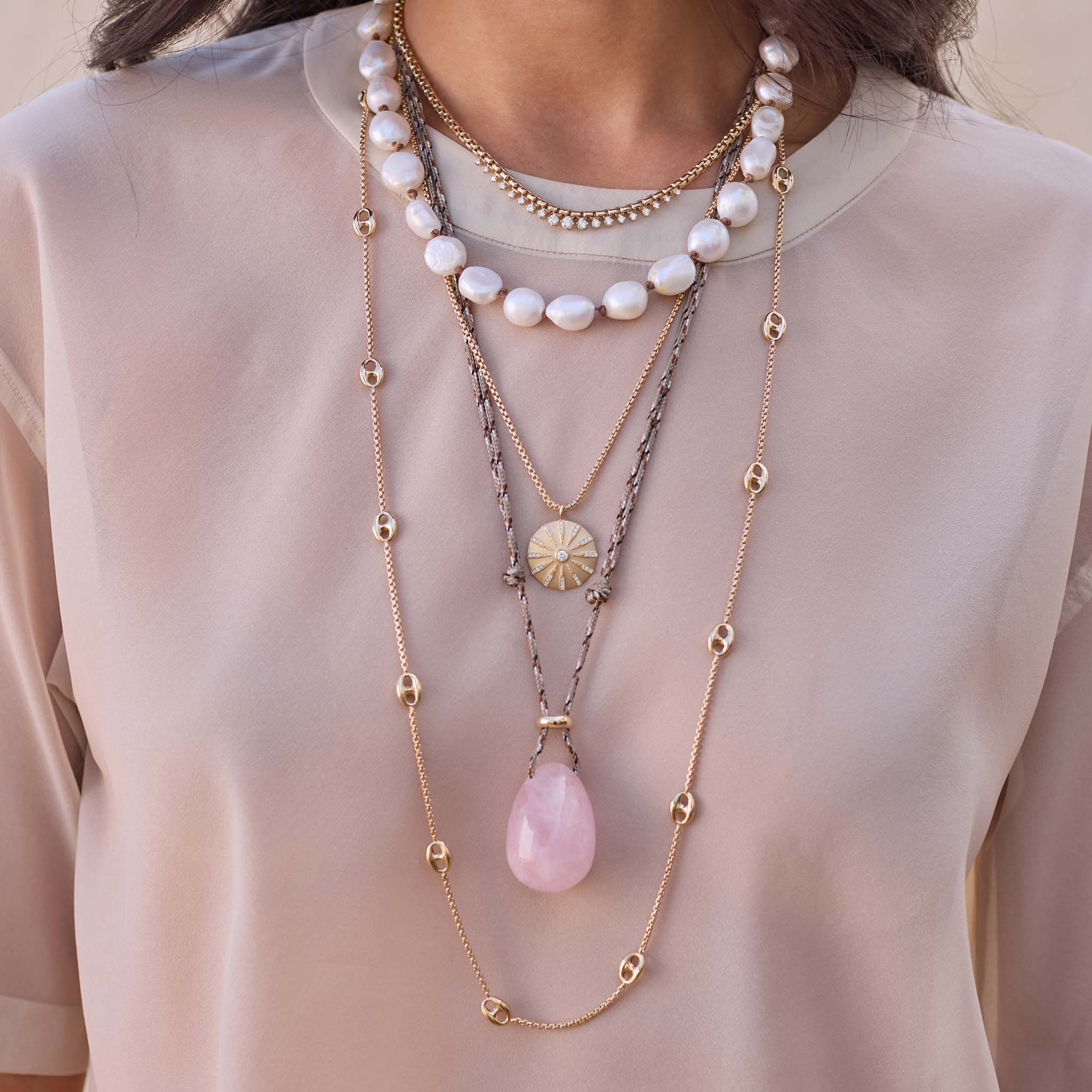 Layered 14k gold Zoe Chicco necklaces with pearls and a pink quartz egg-shaped pendant on a light semi-sheer shirt
