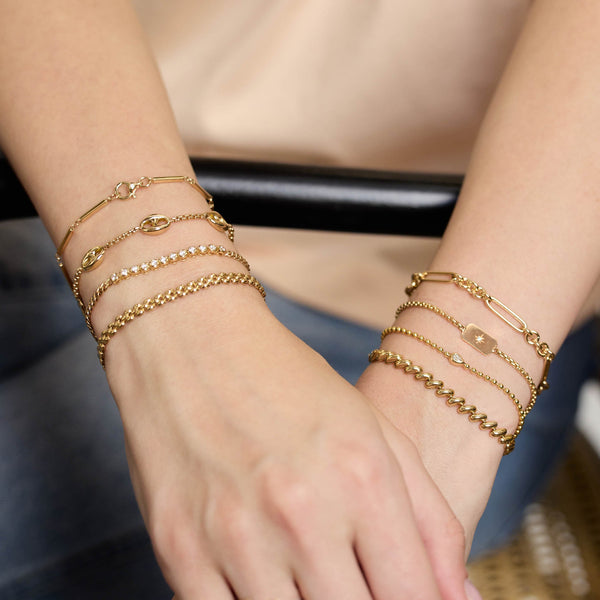 Zoe Chicco 14k gold bracelets on a person's wrist with a blurred background
