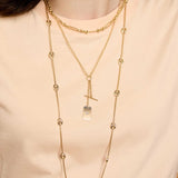 Close up of a person wearing multiple layered Zoe Chicco 14k gold chain necklaces on a light peach background