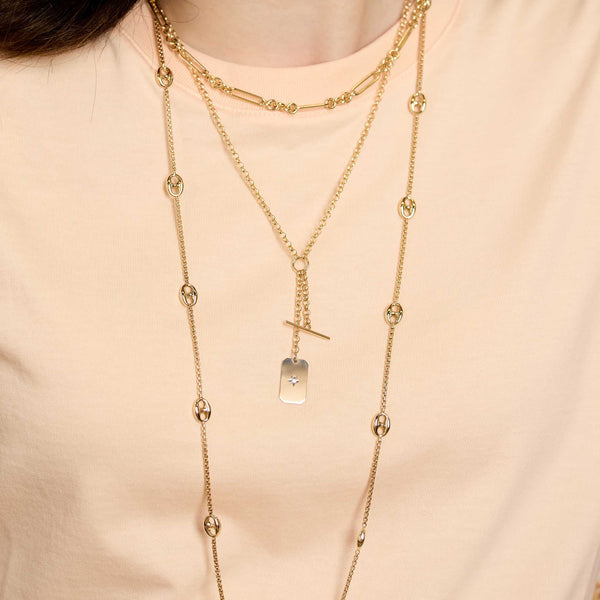 Close up of a person wearing multiple layered Zoe Chicco 14k gold chain necklaces on a light peach background