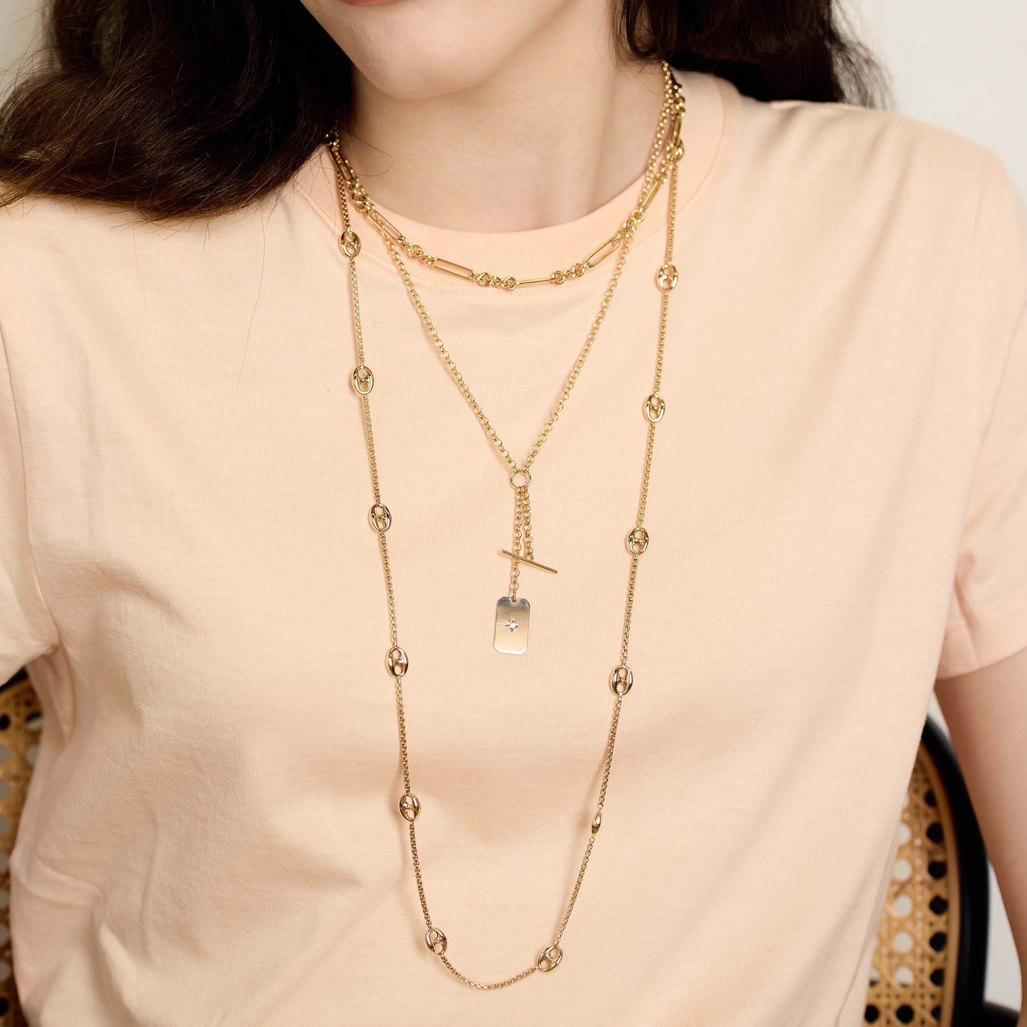 woman in a peach t-shirt wearing a Zoë Chicco 14k Gold 13 Large Mariner Link Station Long Box Chain Necklace layered with a 14k Gold Large Paperclip Rolo Chain Necklace and a Star Set Diamond Square Edge Dog Tag Rolo Chain Lariat