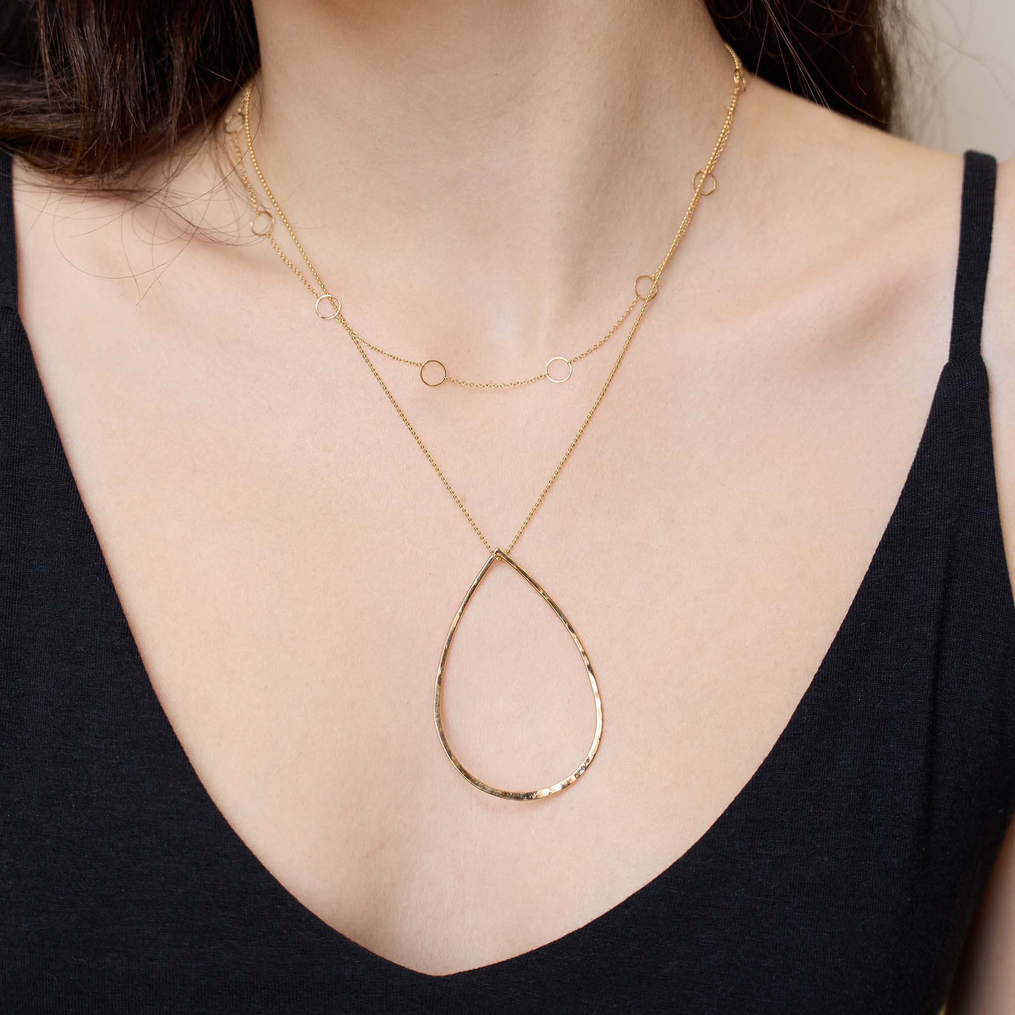 Close up of a person wearing a Zoë  Chicco 14k gold hammered teardrop pendant necklace on white background