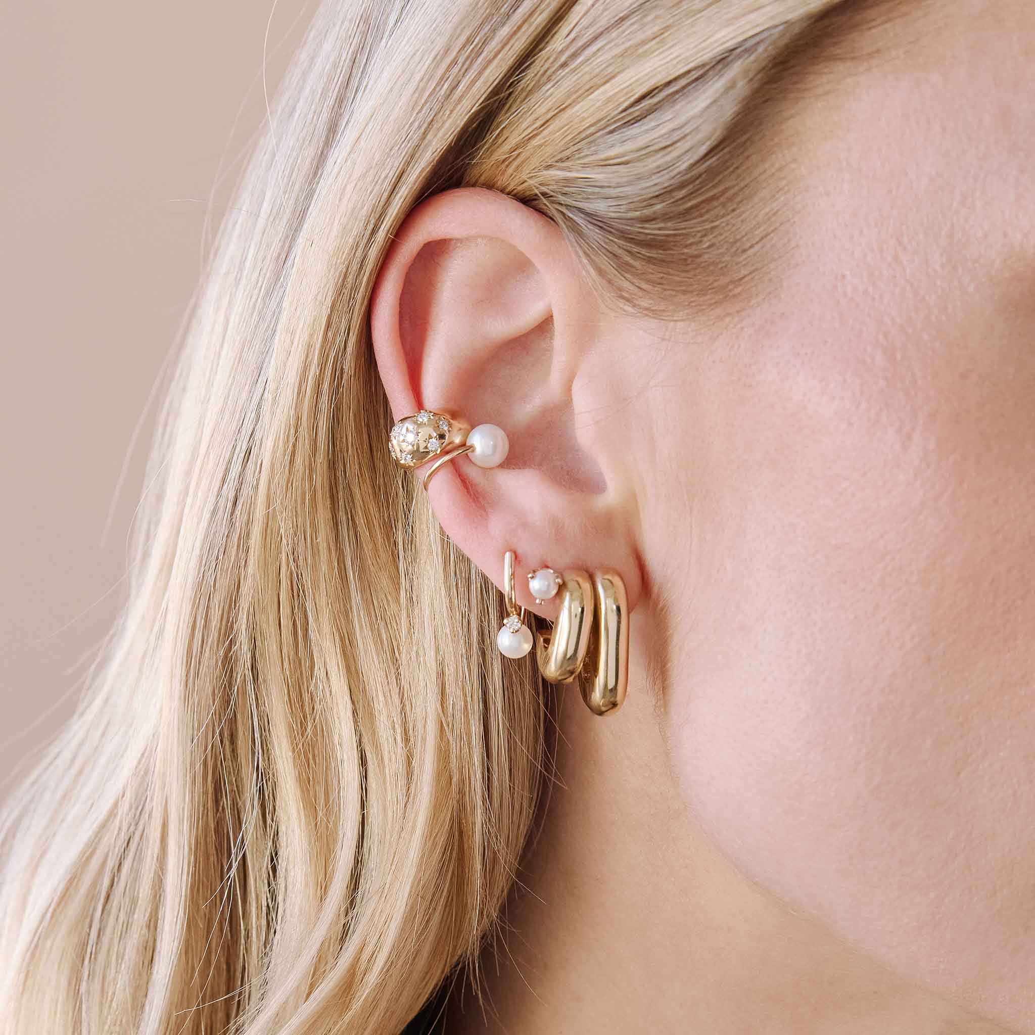 woman's ear wearing a Zoë Chicco 14k Gold Pearl Mixed Double Tube Split Oval Hoop Earring layered with a 14k Prong Diamond Curved Bar Drop & Pearl Jacket Earring and a 14k Double Pearl Ear Cuff and Scattered Star Set Diamond Ear Cuff