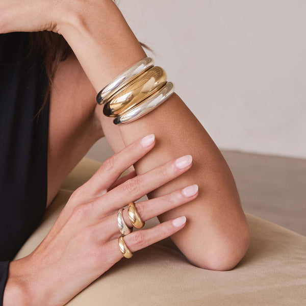 woman resting her elbow on a sofa wearing 2 Zoë Chicco Sterling Silver Medium Aura Cuff Bracelets stacked with a 14k Gold Large Aura Cuff Bracelet on her wrist