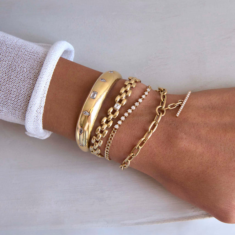 woman's arm against a white background wearing a Zoë Chicco 14k Gold Emerald Cut Diamond Medium Panther Chain Bracelet stacked with a 14k Mixed Cut Diamonds Medium Aura Cuff, 14k Diamond Tennis Segment Small Curb Chain Bracelet, and a 14k Extra Large Square Oval Chain Pavé Diamond Toggle Bracelet