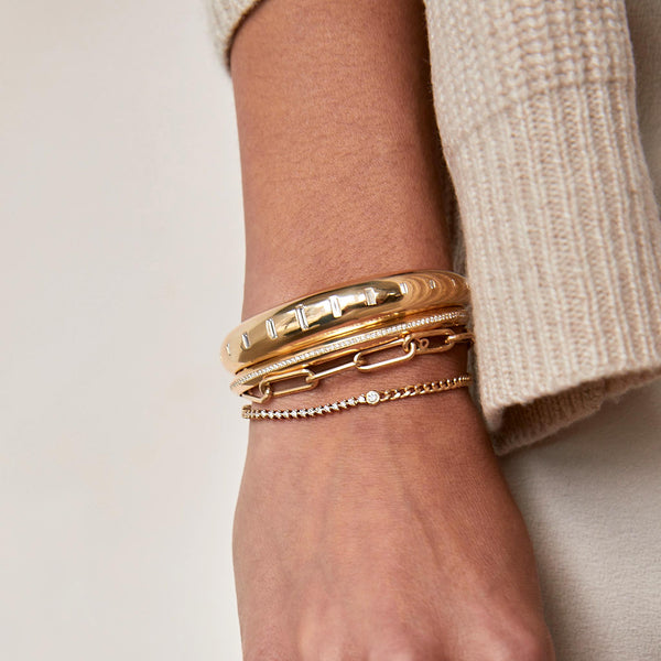 woman's wrist against a beige background wearing a Zoë Chicco 14k Gold Floating Diamond Mixed Curb Chain & Diamond Tennis Bracelet layered with a 14k Graduating Vertical Baguette Diamonds Medium Aura Cuff and a large paperclip link chain bracelet