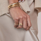 a close up of a woman's hand against beige satin fabric wearing a Zoë Chicco 14k Gold Graduated Prong Diamond Curved Bar Ring stacked with a one of a kind diamond signet ring on her ring finger