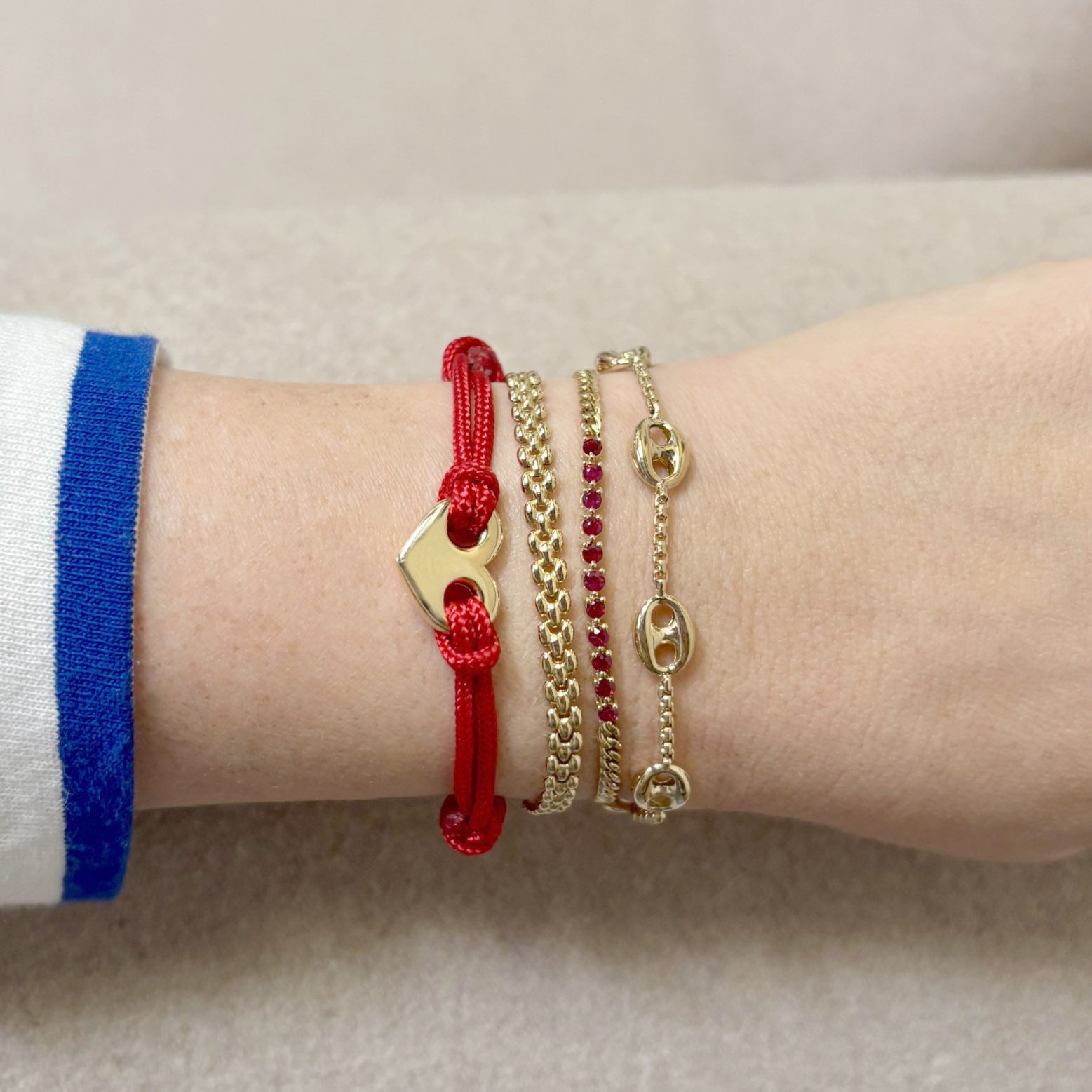 Close-up of a wrist wearing multiple gold and red bracelets on a neutral background